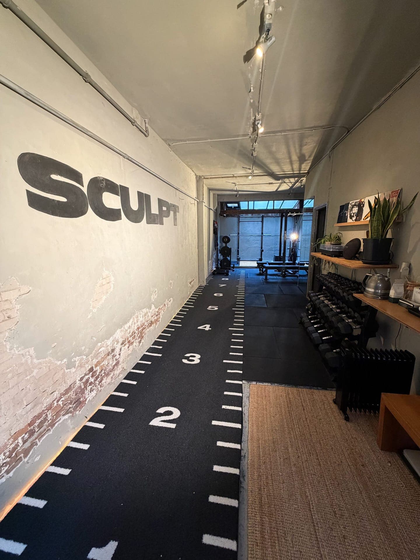 Full overview of the SculptClub private studio in Amsterdam Jordaan — branded sprint lane, dumbbell rack, power rack and canal light